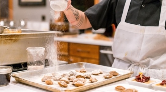 A baker sprinkles icing sugar sugar on his cakes