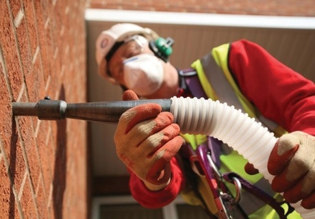 a worker attaches a tube to a brick wall to inject insulation