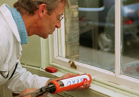 a man uses a glue-gun like apparatus to put draught proofing paste onto a window sill