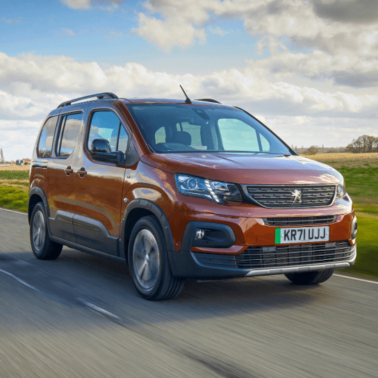Peugeot e-rifter in maroon driving down country road 