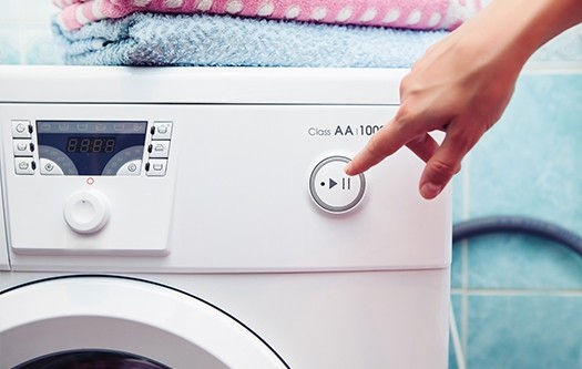 A finger pressing the start button on a washing machine