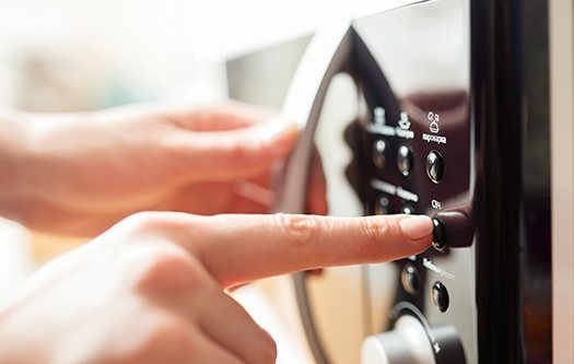 A finger operating the controls of a microwave oven