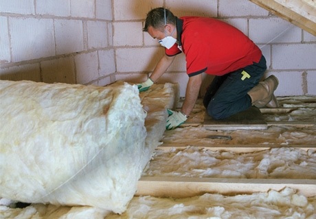 a man wearing a facemask unrolls loft insulation inside a loft