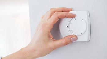 A hand turning a heating thermostat down