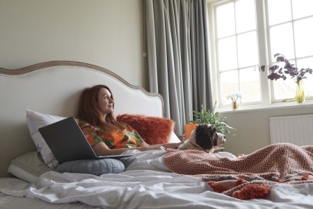 Woman sitting on bed with laptop and dog