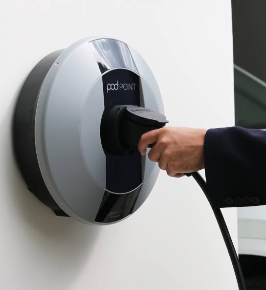 Pod Point charger on wall with hand holding the charge unit
